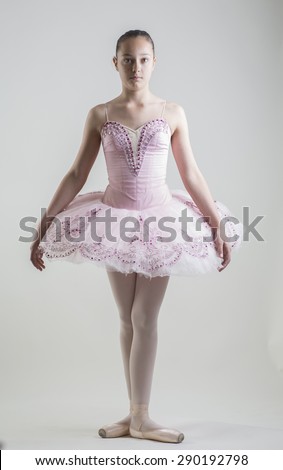 Young ballerina in a pink ballet tutu is dancing on a white background