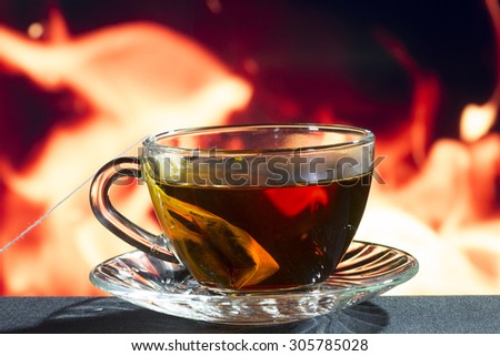 Glass transparent cup with black tea on a background of fire