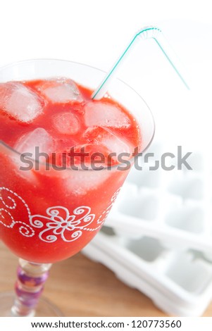 Strawberry smoothie in a cup with straw and ice. Some empty white fridge buckets in the background