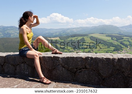 Attractive young caucasian brunette woman looking at the natural landscape from the top of a mountain