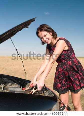 Young woman repairing car, connects cleats to the battery