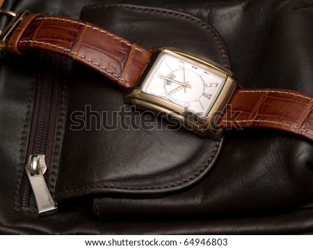 gold watch lying on a leather purse