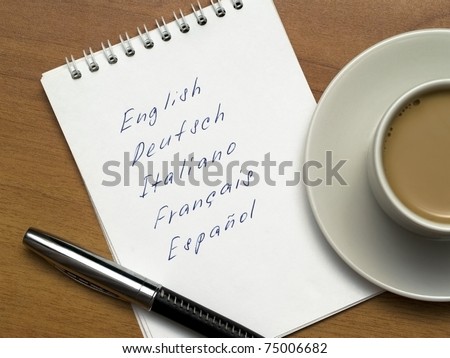multi-languages list in a notebook with a pen and a cup of coffee on a wooden background