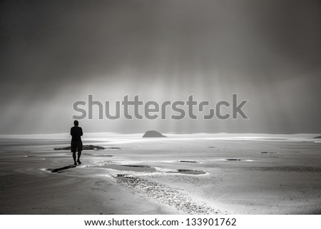 One person walking toward sunbeams on misty beach