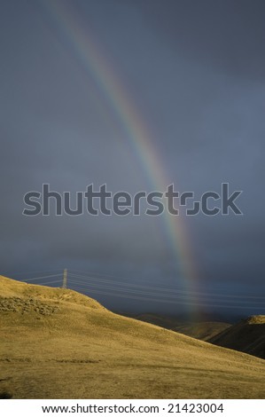 Rainbow above utility lines and sunlit hills