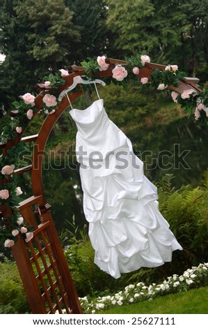 Wedding dress hanging from an arbor decorated with roses
