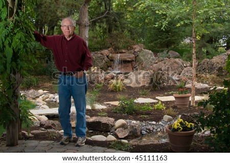 Senior man standing by a man-made pond and waterfall