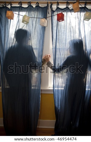Young couple holding hands behind blue curtains.
