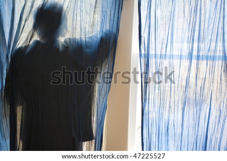 Young man looking out a window behind blue curtains.