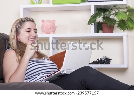 Smiling blonde girl using computer on sofa touching her hair