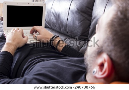 Lying guy using computer on sofa