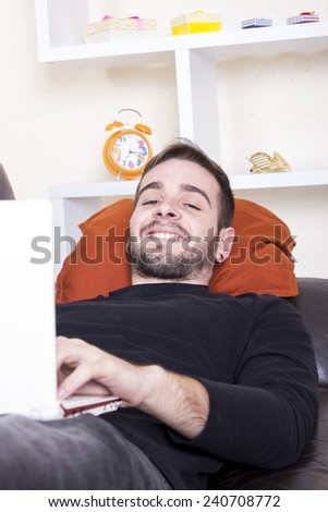 Happy guy using computer lying on sofa