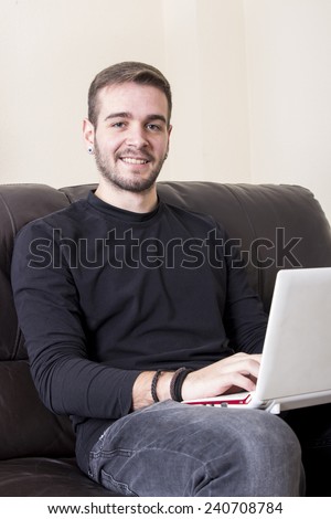 Guy smiling using computer sitting on sofa