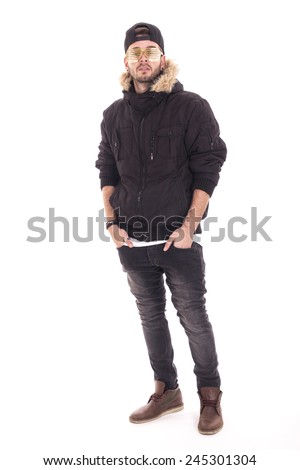 Handsome young guy wearing jacket and black cap with her hands on pockets using gold glasses