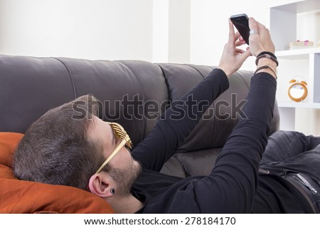 Young guy taking selfie on sofa wearing gold glasses