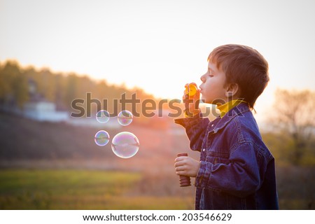 Smiling boy blowing up the soap bubbles on the autumn landscape
