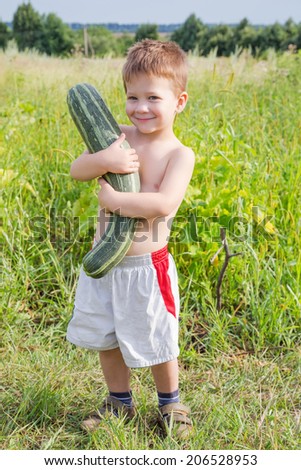 Dirty little boy with zucchini on green patch
