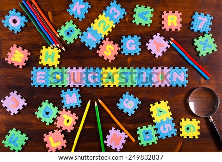 Colorful foam puzzle letters with pencils and lens on wooden background, education concept