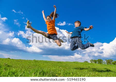 Two happy kids jumping on green hills against blue sky