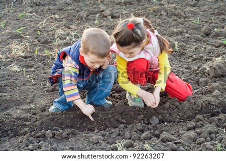 Two little children planting seeds on the field, outdoors