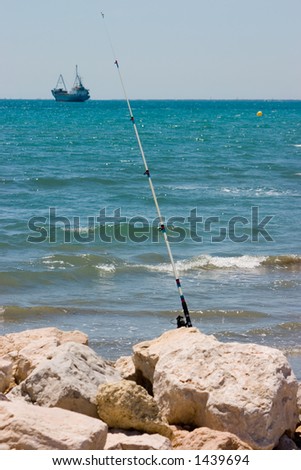 Fishing rod stuck upright in the rocks with line cast into the sea.