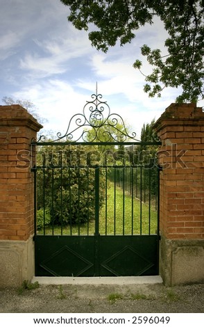 Straight on shot of a nice brick and black wrought iron gate with view of the garden and sky.