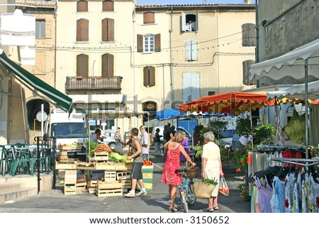An image of French village life on market day showing people, vegetables, clothing.