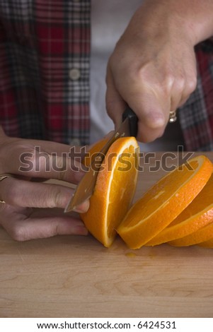 Female hands holding and slicing a fresh orange on a wood cutting board.