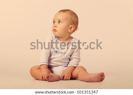 A baby boy in a blue and white bodysuit with a sign Baby Boy, sitting on the floor on the white background