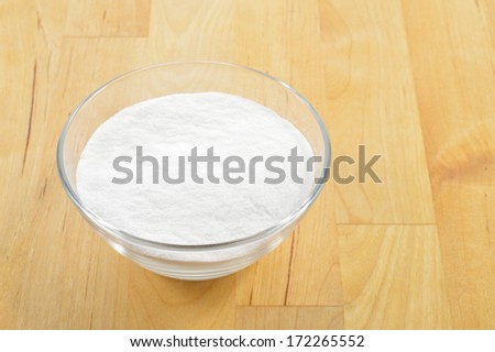 Close-up of baking soda in a glass bowl against background of wooden table. Bicarbonate of soda.
