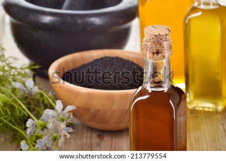 Close-up of nigella sativa oil in a bottle, against of nigella seeds and flowers on wooden background. Black cumin healing herb. Cold pressed, non refined oil. Traditional medicine.