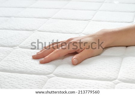 Choosing mattress and bed. Close-up of female hand touching and testing mattress in a store. Copy space.
