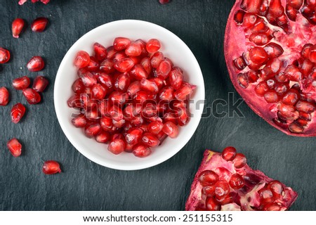 Red pomegranate seeds in a white bowl on table. Open fresh ripe pomegranate. Top view