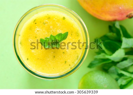 Cooling Mango mint smoothie, summer drink on green table, Yellow Tropical Smoothie made with mango, mint and lime juice.