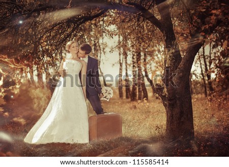 wedding couple with retro suitcase under fall season tree