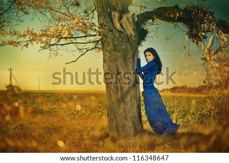 young woman in blue dress under fall season tree