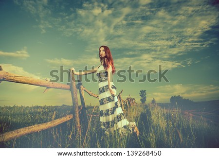young redhead woman at old meadow fence
