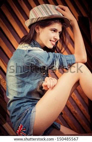 young brunet in jeans clothes and hat at wooden background