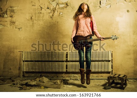 woman jumping with guitar at old dark room