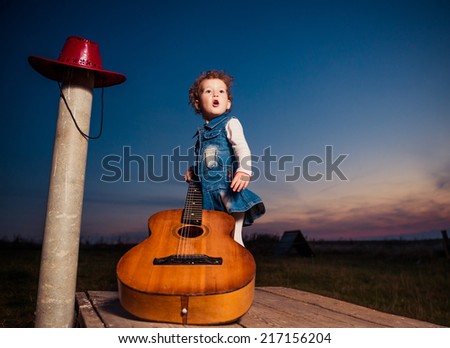 cool girl with big acoustic guitar on a wooden meadow panels at fall sunset