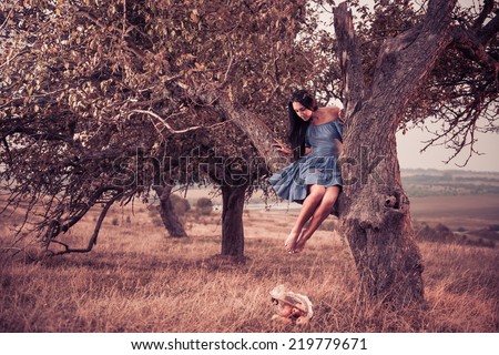 lovely young woman in blue dress on meadow apple tree branch