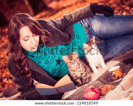 beautiful young lady in coat with two cats reading book on a plaid at fall forest