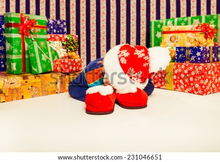 little boy in holiday hat laying indoor with Christmas gifts