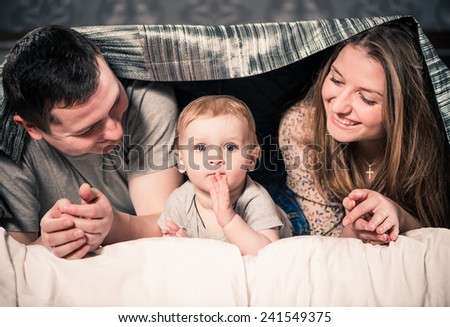happy mother father and little son under bed cover