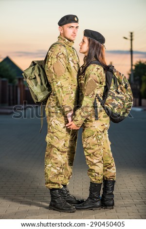 man and woman in military clothes holding hands at sunset street