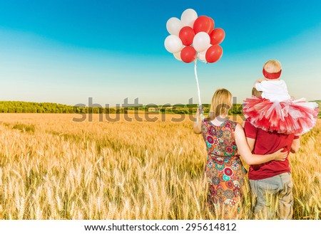 parents with little girl and balloons at wheat field looking at horizon