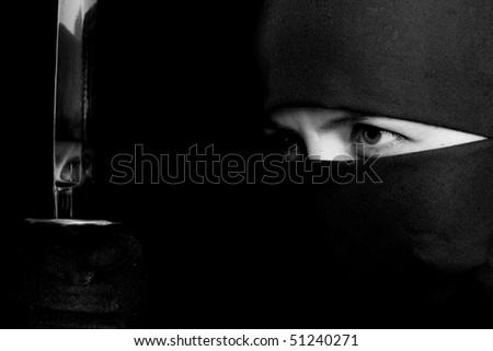 Photo of woman in ninja suit with wakizashi on black background. BW photo