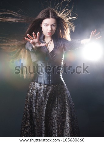 Elegant young witch in a dark clothes cast magic spell