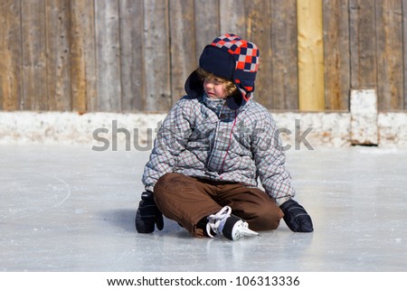 Boy learning to ice skate at an outdoor skating rink in winter.