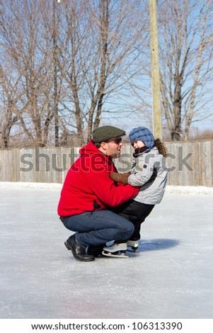 Father teaching daughter how to ice skate at an outdoor skating rink in winter.